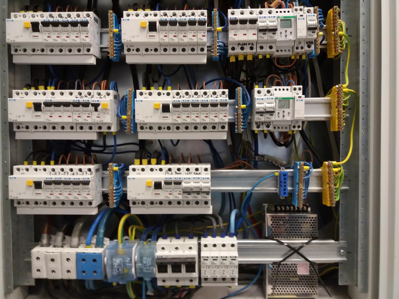 Rozdzielnica elektryczna z zabezpieczeniami nadprądowymi Eaton, widoczne przewody w kolorach niebieskim, żółtym i czarnym oraz listwy zaciskowe.