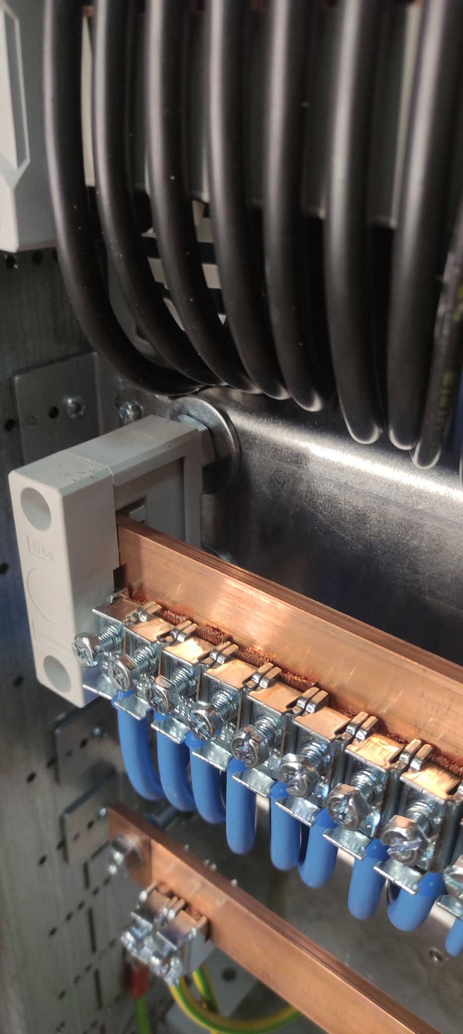 Szyna wyrównawcza potencjałów z podłączonymi przewodami ochronnymi w rozdzielnicy elektrycznej, widoczne śruby mocujące i przewody w niebieskiej izolacji.