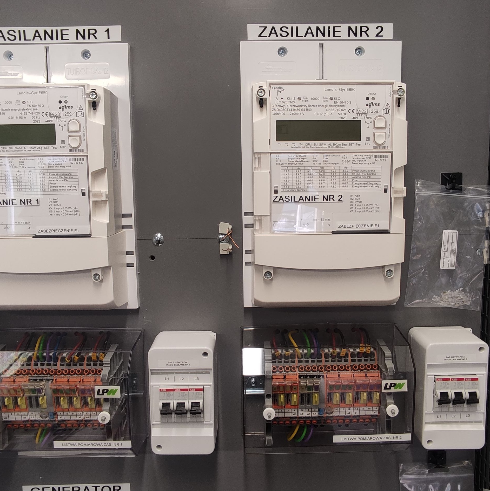 Szara tablica rozdzielcza z dwoma licznikami energii elektrycznej z napisem Zasilanie NR 1 i Zasilanie NR 2, zabezpieczeniami F1 oraz listwami pomiarowymi WAGO ZASILANIE NR 1 i NR 2, widoczne...