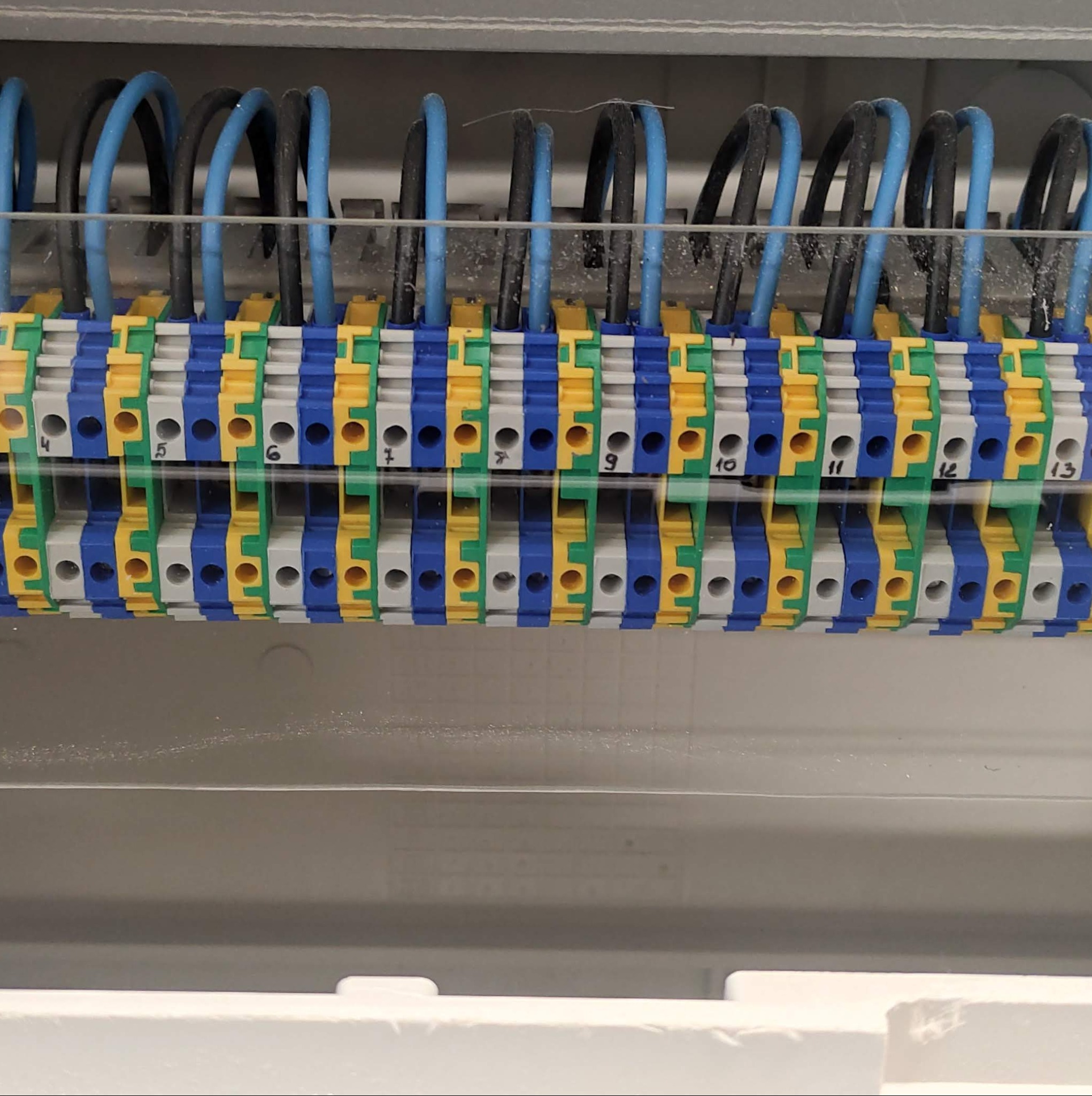 Szyna zaciskowa w rozdzielnicy elektrycznej z podłączonymi przewodami w kolorach niebieskim i czarnym, numery zacisków od 4 do 13.