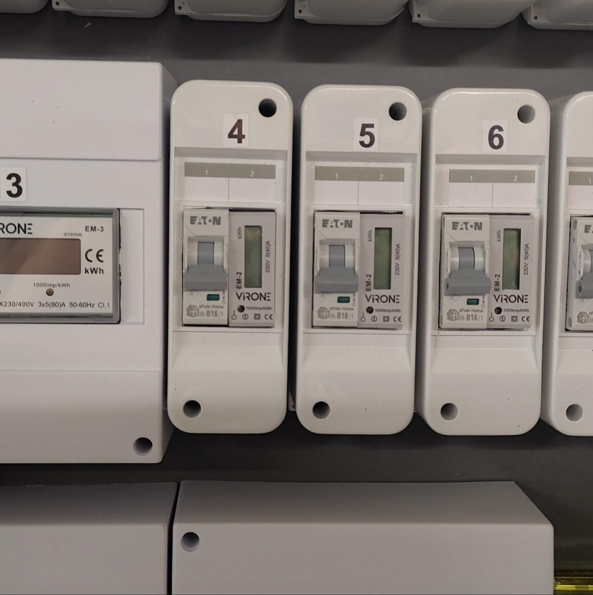 Szczegółowe ujęcie tablicy rozdzielczej z kilkoma licznikami energii elektrycznej, oznaczonymi numerami 3, 4, 5 i 6, z widocznymi parametrami technicznymi i logo producentów.