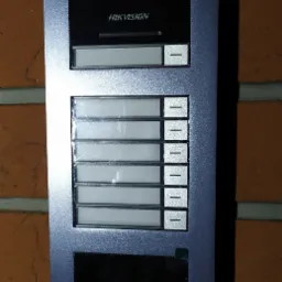 Zamontowany na ceglanej ścianie, wielorodzinny panel domofonowy Hikvision z kamerą, sześcioma przyciskami wywoławczymi i czytnikiem kart.