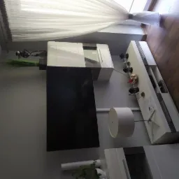 Nowoczesna aranżacja salonu z białymi szafkami wiszącymi i podłogowymi, telewizorem na ścianie, lampą stojącą z białym abażurem i drewnianą podłogą.