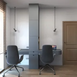 Dwa stanowiska pracy z szarymi biurkami i krzesłami obrotowymi, oddzielone szarą kolumną z półkami i szufladami, oświetlone punktowymi lampami sufitowymi, z laptopem na jednym z biurek i żaluzjami...