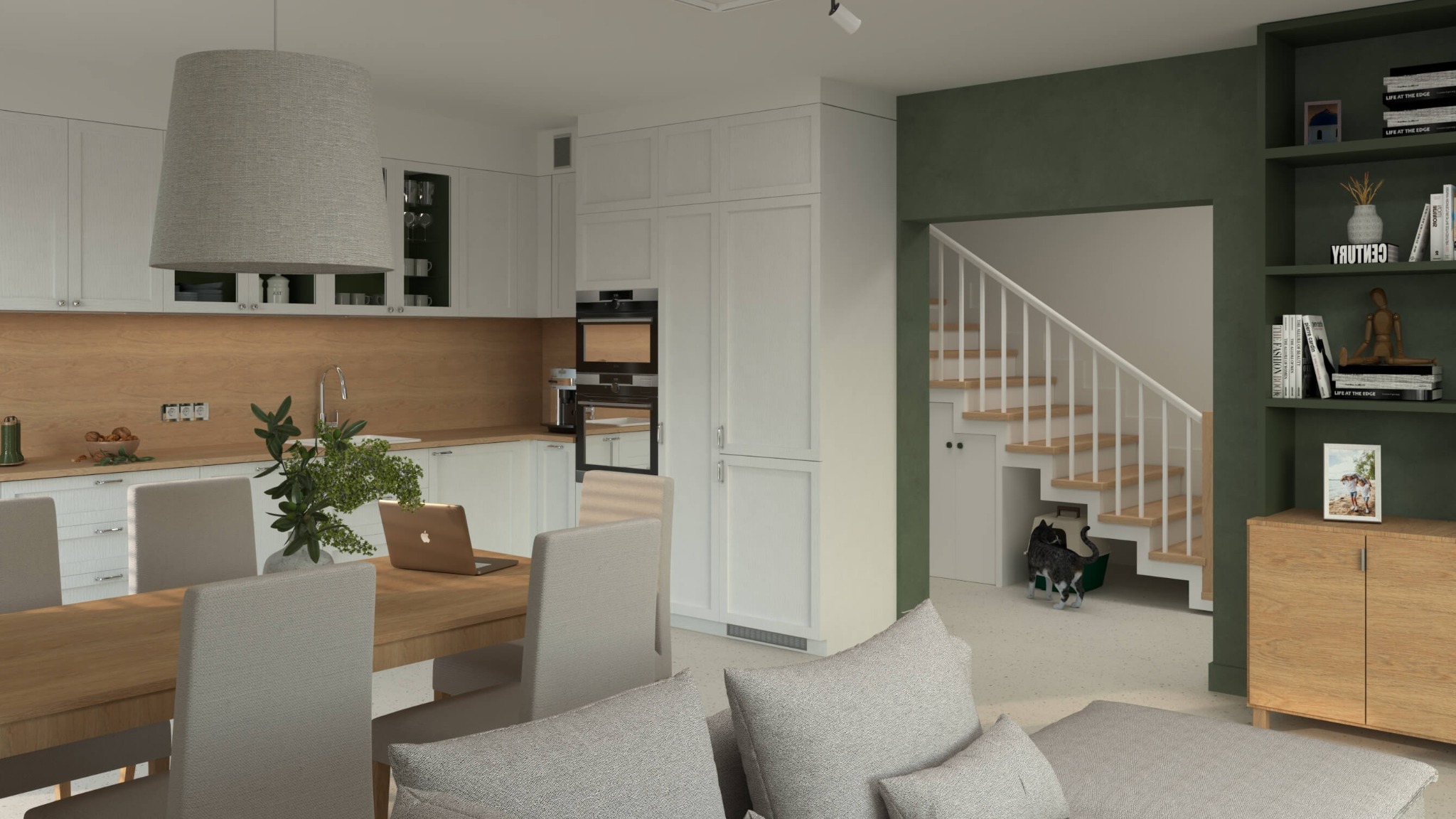 Wnętrze domu z otwartą kuchnią, jadalnią i schodami; białe szafki kuchenne, drewniany blat, stół z laptopem, szara lampa nad stołem, zielona ściana z regałem, kot w pobliżu schodów.