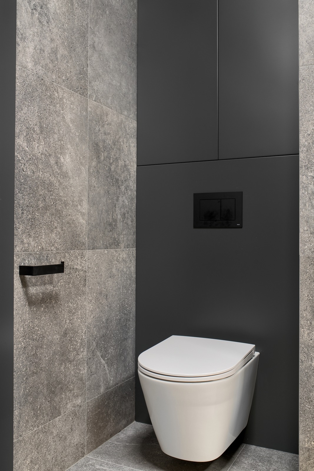 Nowoczesna toaleta wisząca z szarą, kamienną okładziną ścienną i czarną zabudową. Minimalistyczny design, eleganckie wykończenie.