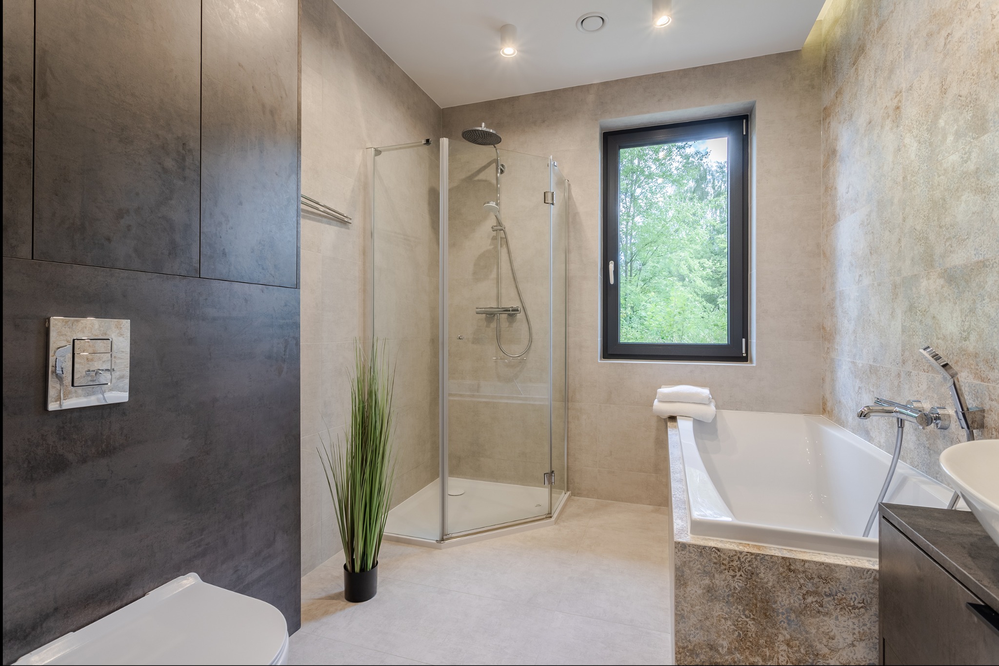Nowoczesna łazienka z kabiną prysznicową, wanną i oknem z widokiem na zieleń. Neutralna kolorystyka, minimalistyczny design i oświetlenie punktowe.