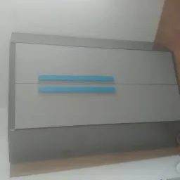 Dwudrzwiowa szafka w odcieniach szarości z poziomymi, błękitnymi uchwytami na tle ściany i podłogi z paneli.