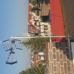 Antena telewizyjna zamontowana na kominie, widok z góry na tle błękitnego nieba i zabudowań miejskich.