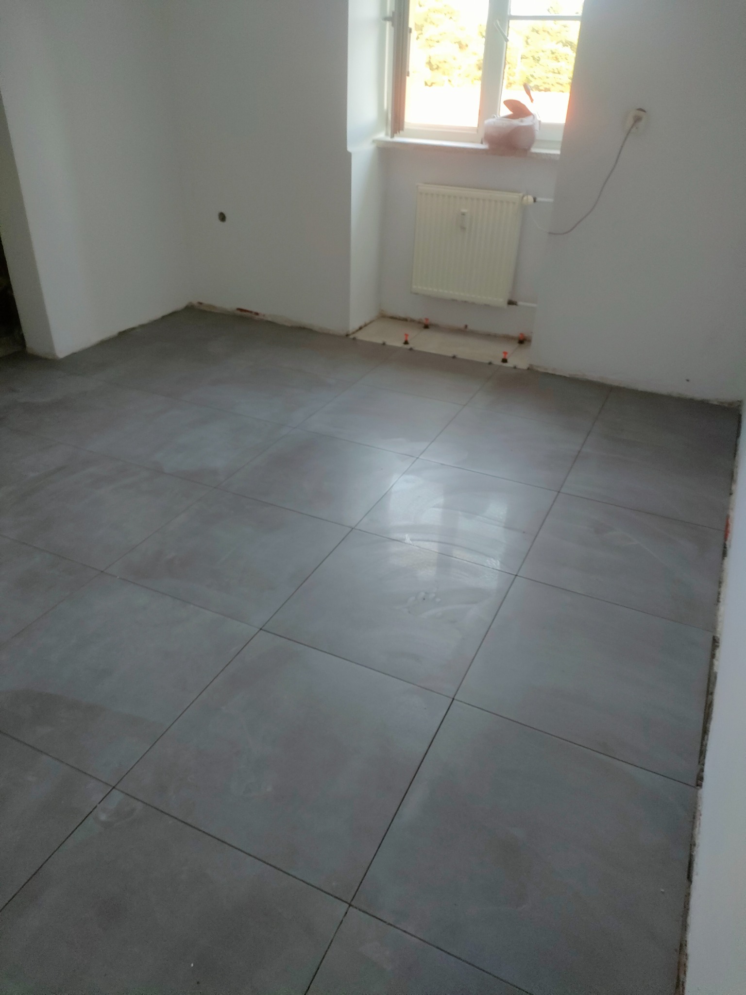 Układanie szarych płytek podłogowych w pomieszczeniu w Bydgoszczy, widoczne plastikowe krzyżyki dystansowe, przygotowanie do fugowania.