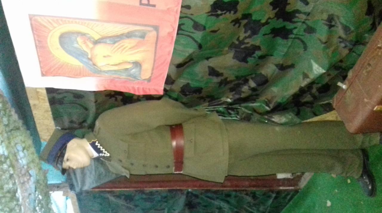 Manekin w mundurze wojskowym z epoki, z obrazem religijnym w tle i plandeką w kamuflażu.