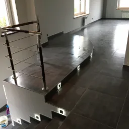 Nowoczesne wnętrze z ciemną, błyszczącą podłogą z płytek, schody z oświetleniem LED w stopniach i metalową balustradą z drewnianymi elementami, widok z góry.