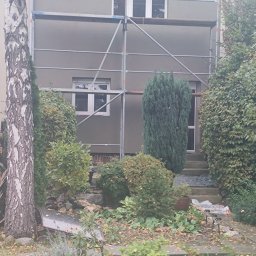ELEWACJE Sławomir Leja - Dom jednorodzinny w trakcie tynkowania elewacji, widoczne rusztowanie, świeżo nałożony szary tynk, ogród z liśćmi jesiennymi na pierwszym planie.