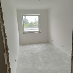ELEWACJE Sławomir Leja - Pokój po nałożeniu pierwszej warstwy gładzi, widoczne ślady po szpachlowaniu na podłodze, wystające kable ze ściany i niedokończone obramowanie drzwi.
