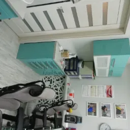 Nowoczesny gabinet stomatologiczny z dwoma fotelami dentystycznymi, turkusowymi szafkami i białymi ścianami ozdobionymi zdjęciami i kalendarzem.