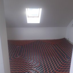 Hydro-Net - Czerwone rury ogrzewania podłogowego ułożone na czarnej izolacji w pokoju z oknem dachowym, widok z góry.