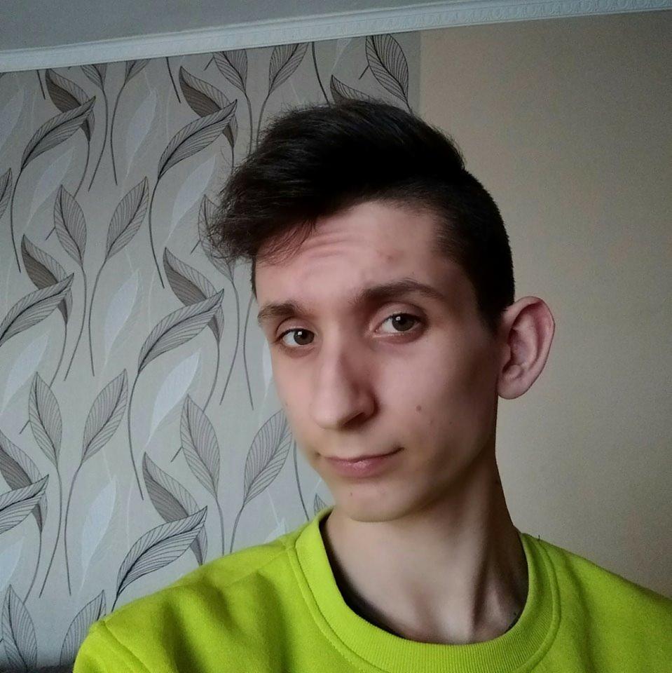 Portret młodego copywritera z Bobrowej w neonowej bluzie na tle tapety w liście. Wyraz twarzy: lekki uśmiech, patrzący w obiektyw, naturalne oświetlenie.