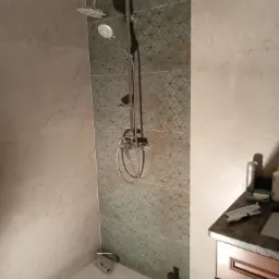 Wykończona kabina prysznicowa z dwoma rodzajami płytek: szare imitujące kamień i turkusowe z geometrycznym wzorem, chromowana bateria prysznicowa z deszczownicą i słuchawką, odpływ liniowy w podłodze.