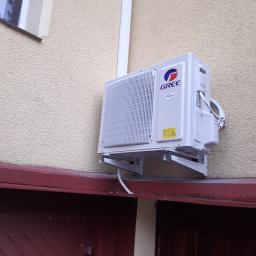 Mikart - Zewnętrzna jednostka klimatyzatora marki Gree zamontowana na elewacji budynku, widoczna rura odprowadzająca skropliny i przewody.