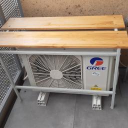 Mikart - Zewnętrzna jednostka klimatyzacji GREE zamontowana na metalowym stelażu z drewnianymi blatami, stojąca na balkonie.