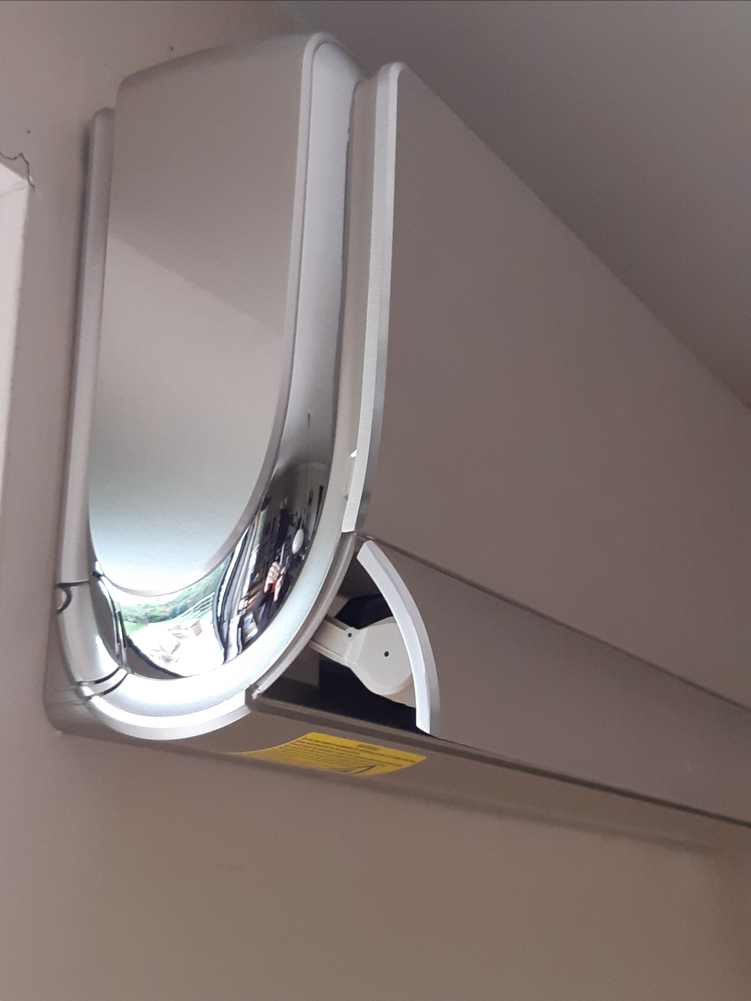 Nowoczesny, biały klimatyzator z chromowanymi elementami, zamontowany na beżowej ścianie, widok z dołu.