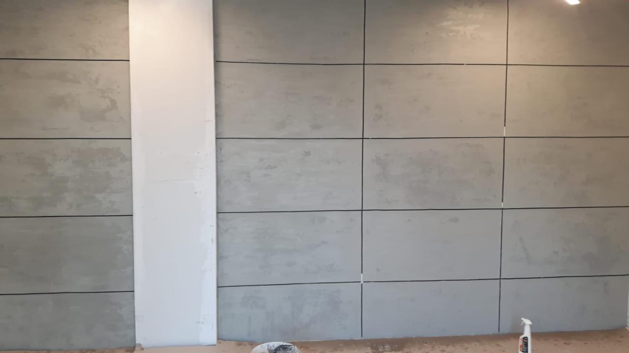 Ściana wykończona panelami imitującymi beton, z widoczną białą kolumną i narzędziami na podłodze.