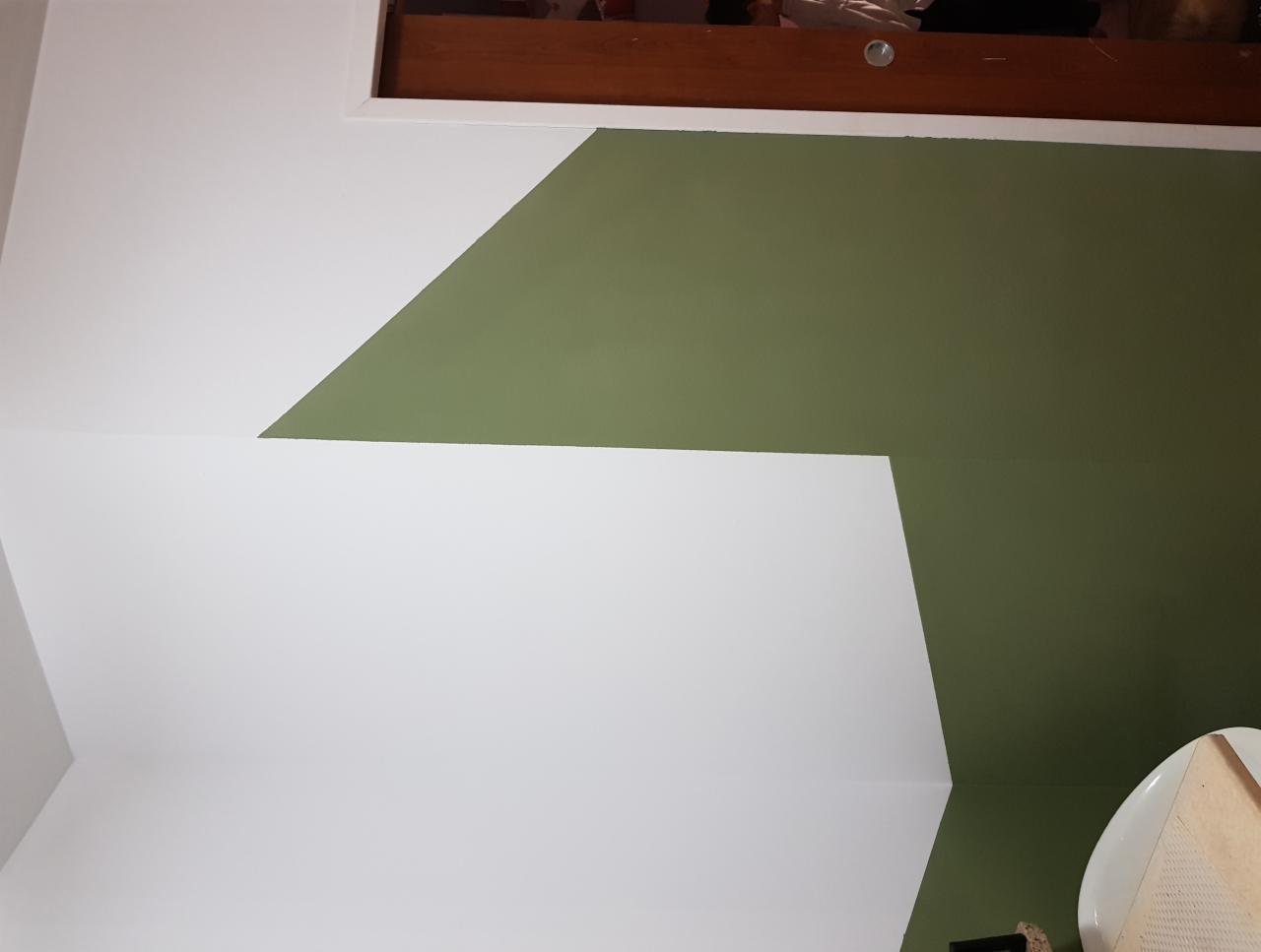 Ściana pomalowana na biało i oliwkowo z widocznym fragmentem sufitu i drewnianej ramy okiennej.