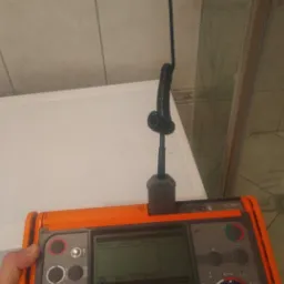 Miernik Sonel MPI-520 podłączony do gniazdka elektrycznego podczas pomiarów, widoczna ręka osoby trzymającej urządzenie.