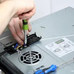 Podłączenie przewodów do płyty indukcyjnej za pomocą śrubokręta z zieloną rączką. Widoczne kolorowe kable, czarna obudowa przyłącza, instrukcja schematyczna na obudowie płyty i narzędzia.