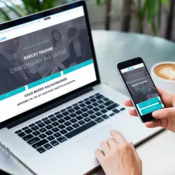 Responsywna strona internetowa firmy z Gdyni wyświetlana na laptopie i smartfonie, z logo i hasłem 'Rzeczy trudne zamieniamy na łatwe', obok filiżanka cappuccino.