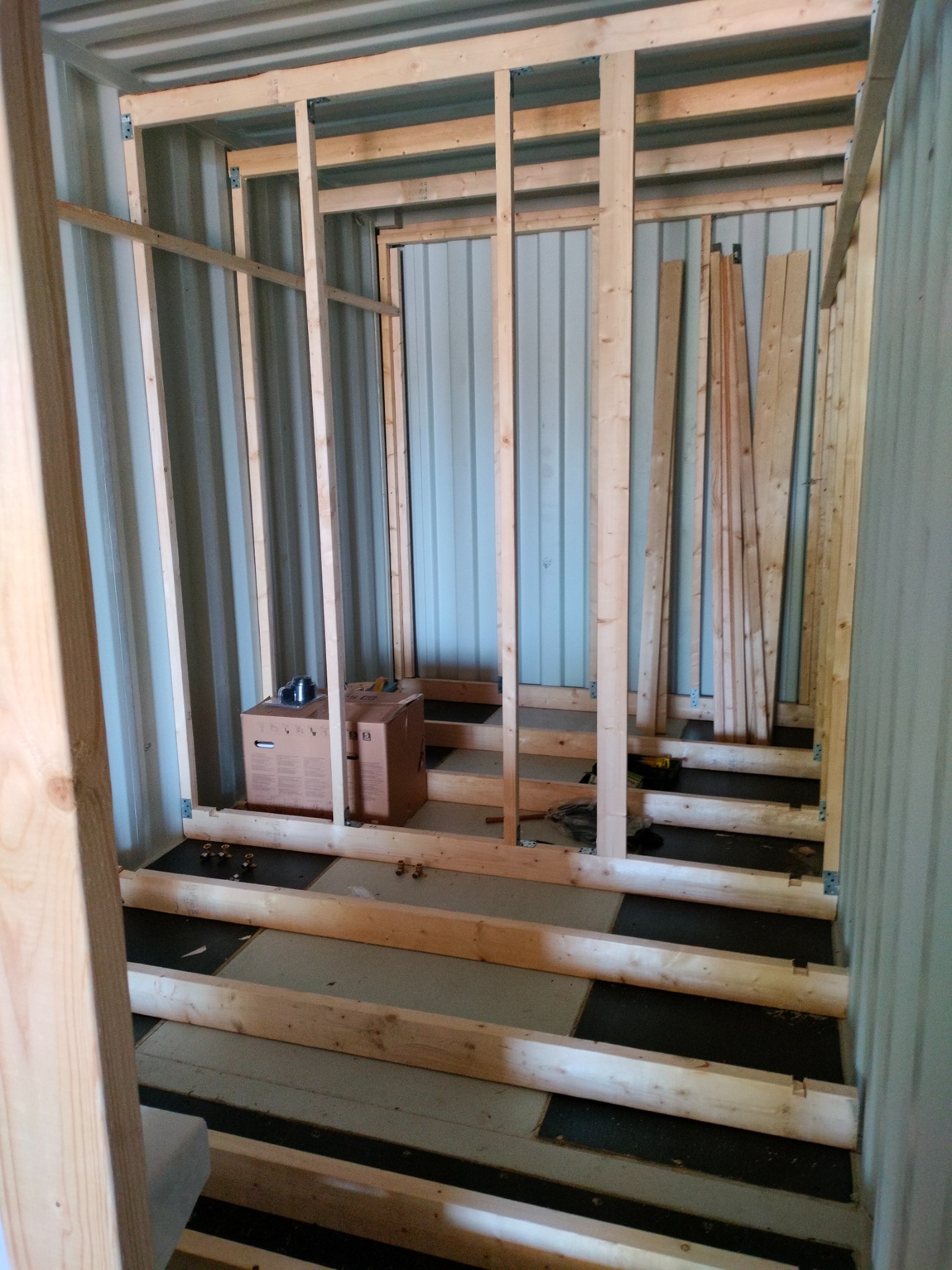 Wnętrze kontenera po adaptacji: drewniany szkielet ścian i podłogi, widoczne materiały izolacyjne i narzędzia. Etap prac instalacyjnych w kontenerze.