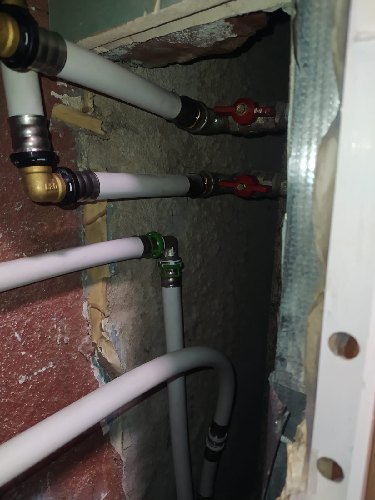 Białe rury instalacji wodnej z zaworami, widoczne połączenia i elementy miedziane, zamontowane w ścianie z widocznymi śladami po kuciu.