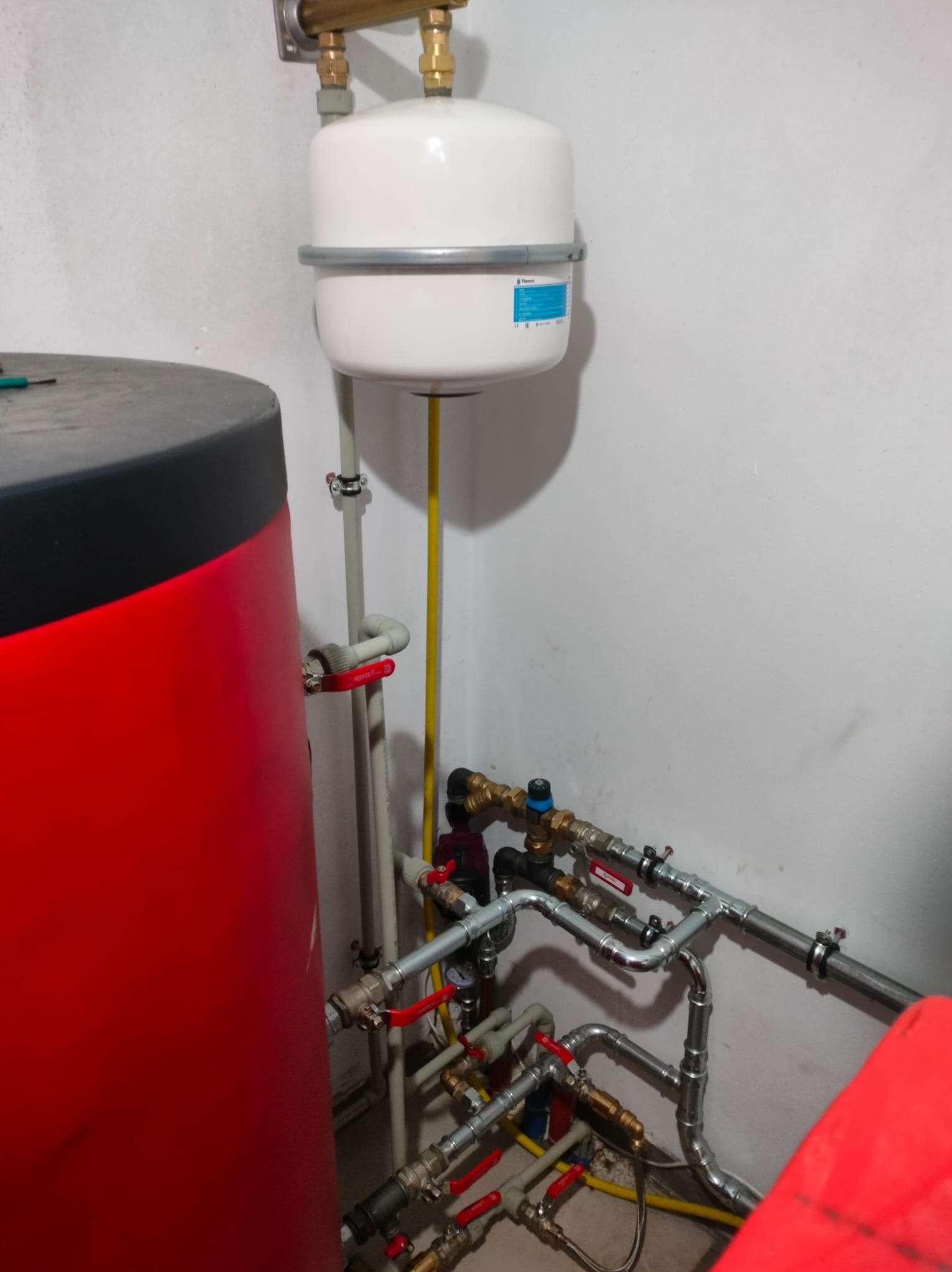 Czerwony zbiornik CO, biały zbiornik wyrównawczy i instalacja z rur miedzianych z zaworami w kotłowni. Widoczne połączenia i elementy instalacji grzewczej.