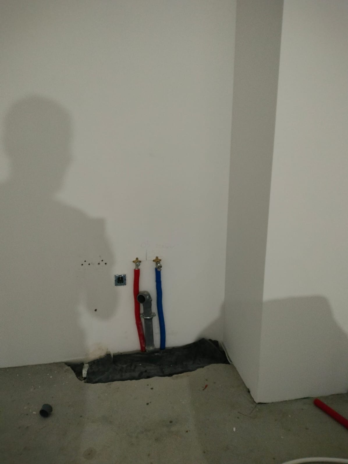 Przyłącza wodne z rurami PEX w kolorze czerwonym i niebieskim, wystające ze ściany w Orlu. Widoczne ślady po kuciu w ścianie i podłodze. Instalacja w trakcie prac.