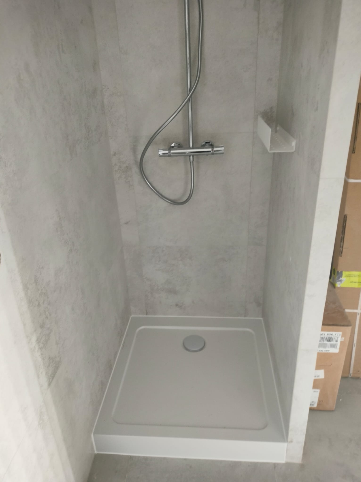 Nowoczesna kabina prysznicowa z szarymi płytkami imitującymi kamień, chromowaną armaturą i minimalistyczną półką. Widok z góry na brodzik.