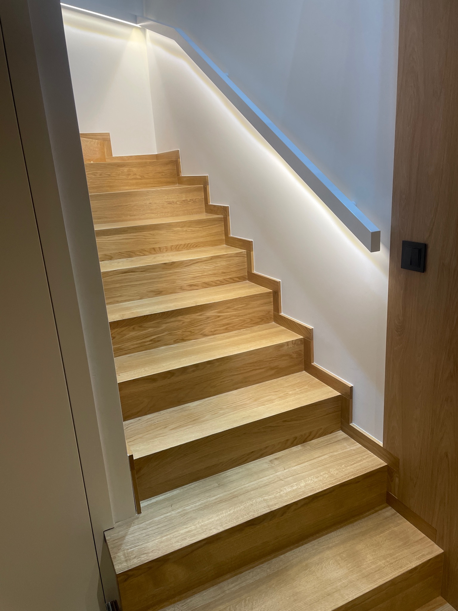 Nowoczesne schody z jasnego drewna z podświetleniem LED wzdłuż ściany, widok z dołu.