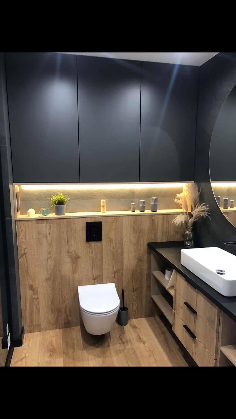 Nowoczesna łazienka z drewnopodobnymi panelami, podświetlaną półką z dekoracjami, wiszącą toaletą i umywalką nablatową.