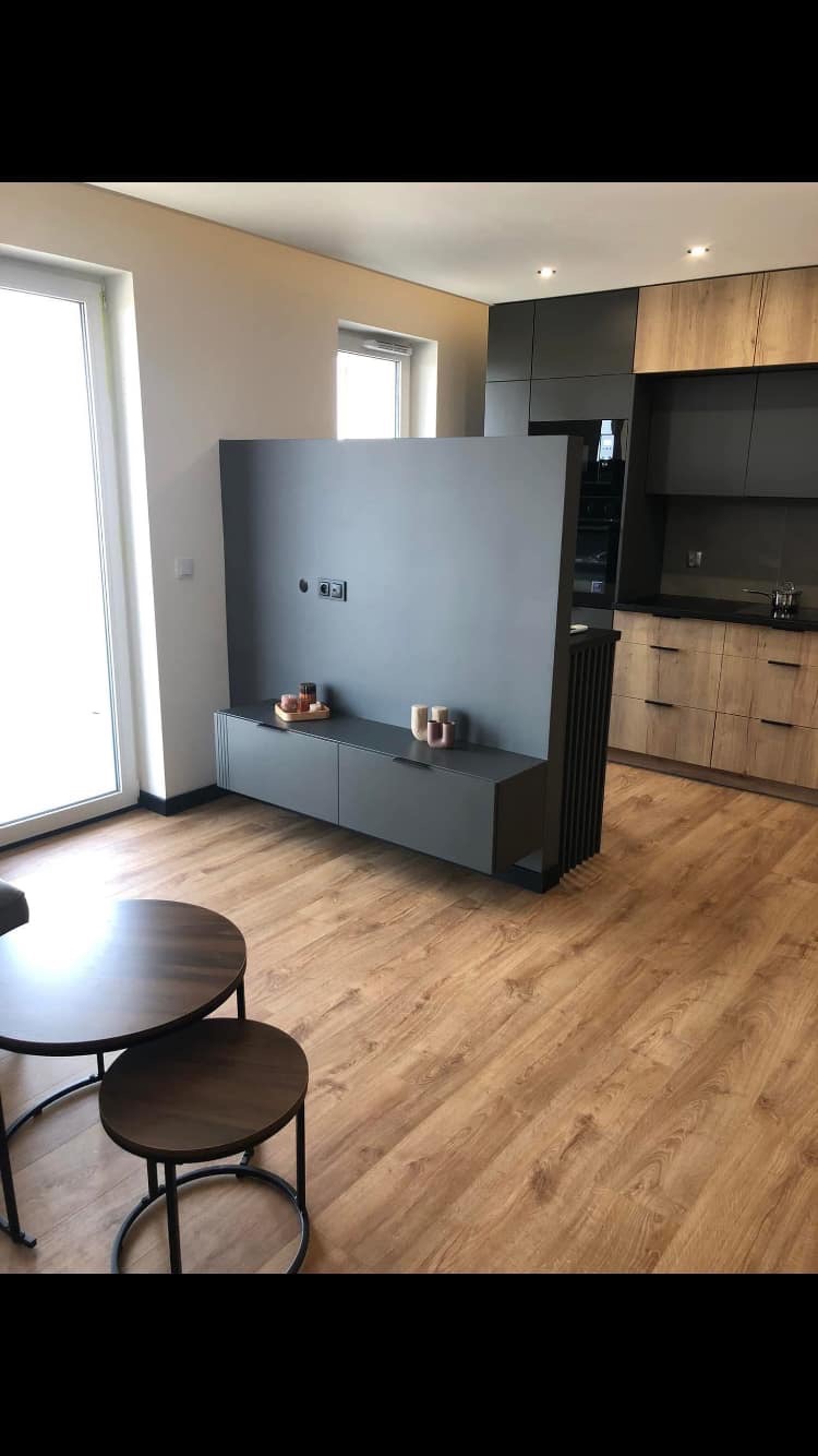 Nowoczesne wnętrze: szara ściana działowa z szafkami RTV oddzielająca salon od kuchni z drewnianymi frontami, podłoga z paneli, okrągłe stoliki kawowe w salonie.