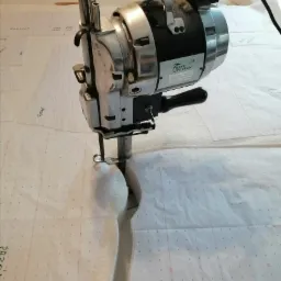 Elektryczny nóż krawiecki tnący grubą warstwę materiału, widoczne szablony z naniesionymi wymiarami.