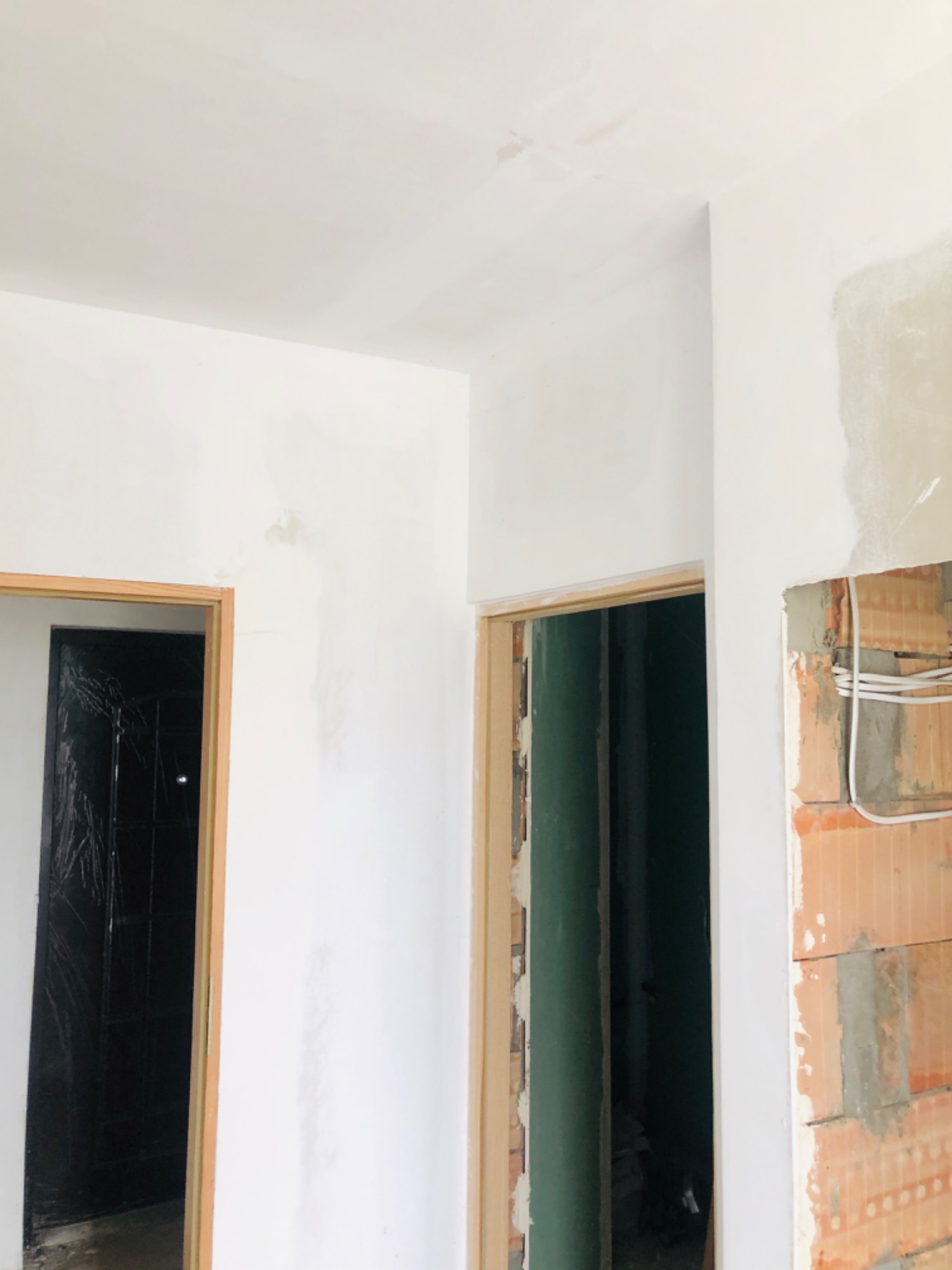 Wnętrze w trakcie prac wykończeniowych: widoczne ościeżnice drzwiowe, fragment ściany z cegły z instalacją elektryczną oraz pomalowane ściany i sufit na biało.