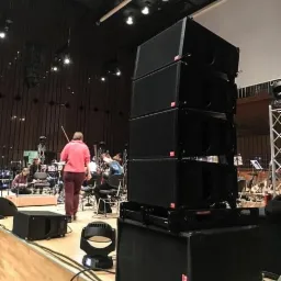 Scena z ustawionym systemem nagłośnieniowym line array przed orkiestrą, widoczny również reflektor sceniczny.