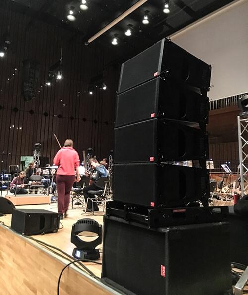 Scena z ustawionym systemem nagłośnieniowym line array przed orkiestrą, widoczny również reflektor sceniczny.