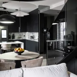 Nowoczesna kuchnia w odcieniach szarości i czerni z marmurowym blatem, okrągłym stołem z owocami i designerskimi lampami wiszącymi.