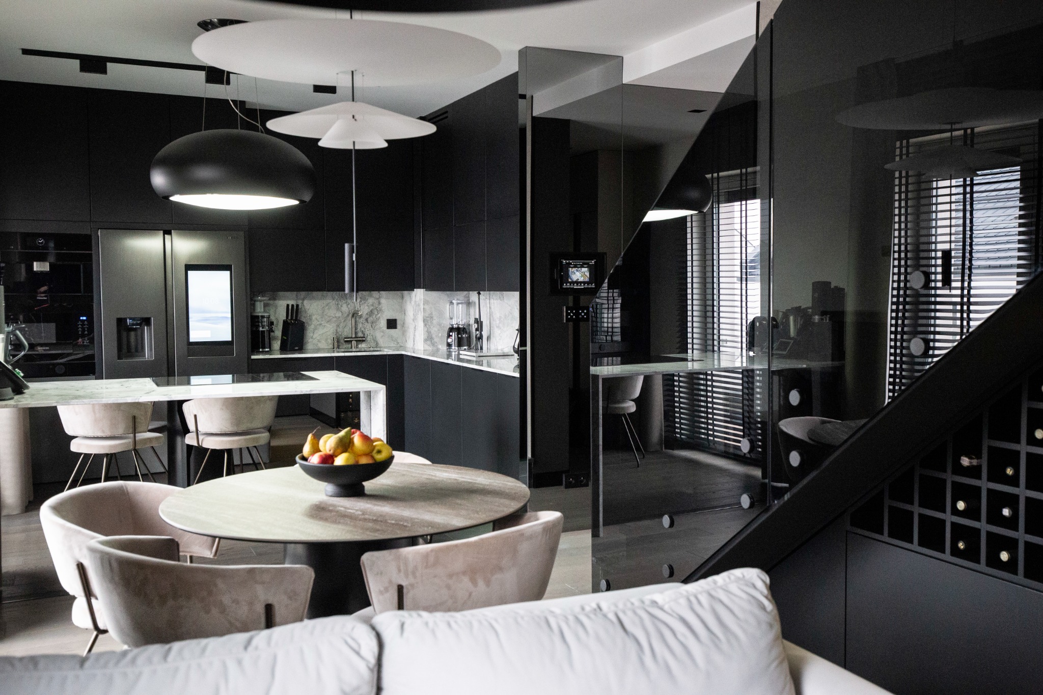 Nowoczesna kuchnia w odcieniach szarości i czerni z marmurowym blatem, okrągłym stołem z owocami i designerskimi lampami wiszącymi.
