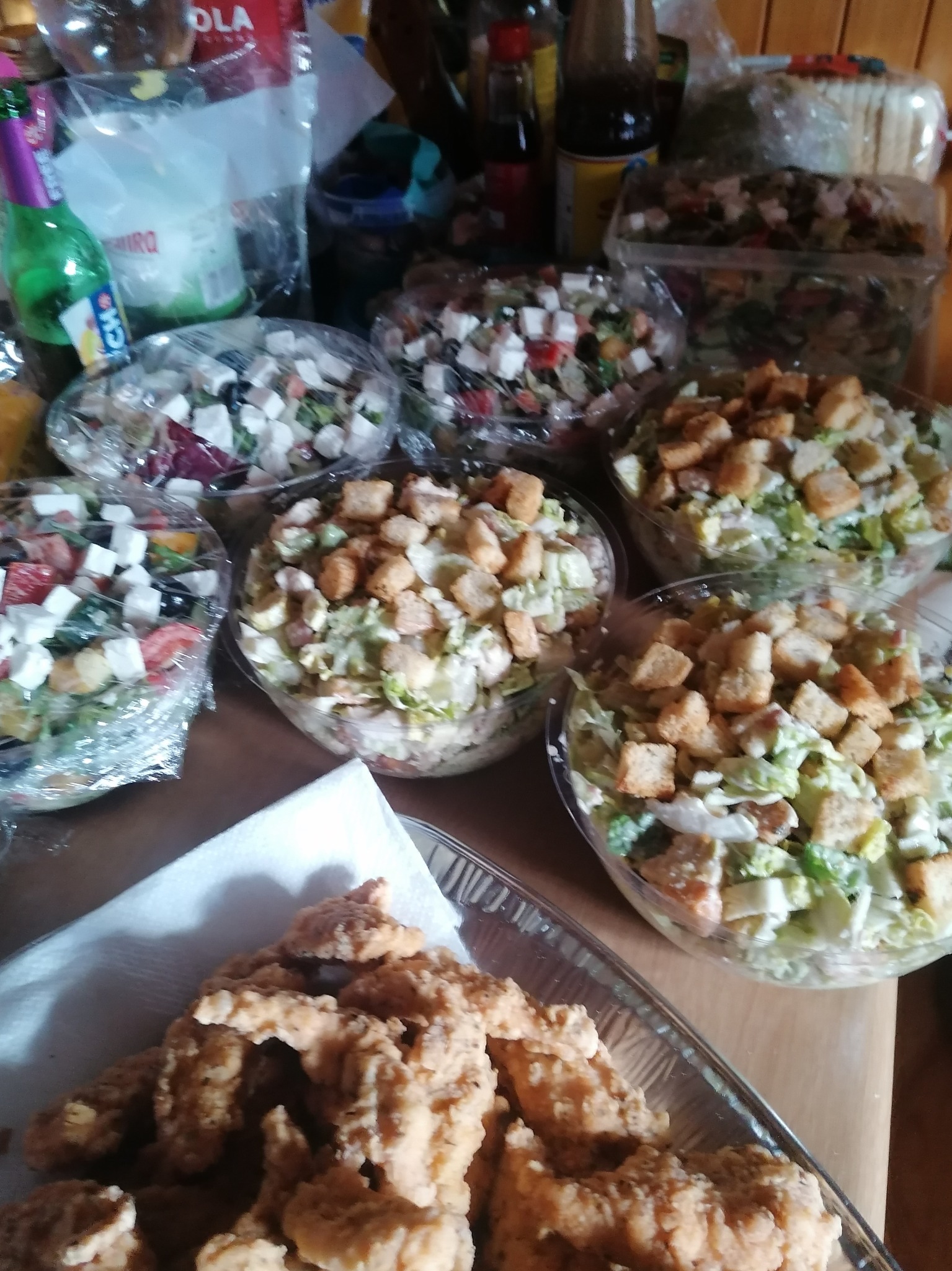 Przygotowane sałatki greckie i Cezar w przezroczystych miskach oraz smażone kawałki kurczaka na tacy, gotowe do serwowania.