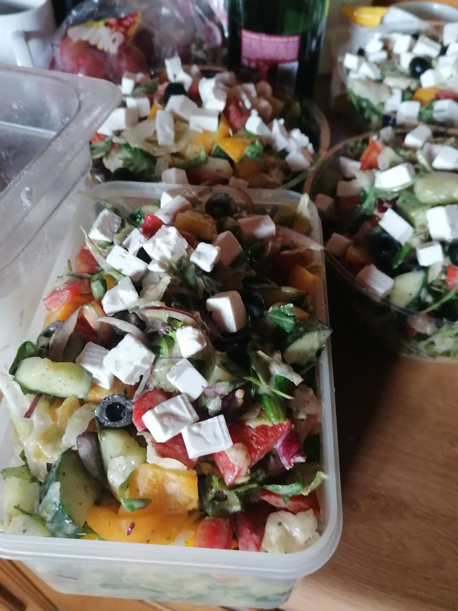 Sałatka grecka z serem feta, ogórkiem, pomidorem, papryką i oliwkami w przezroczystych pojemnikach, przygotowana do transportu.