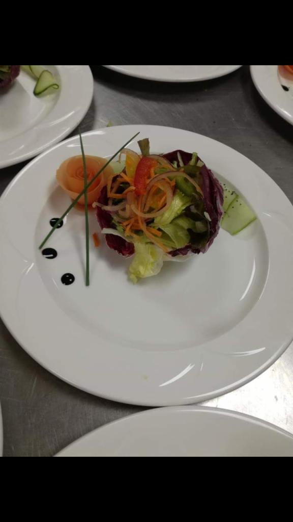 Elegancko podana sałatka z warzyw w liściu sałaty radicchio, ozdobiona rozetką z marchewki i kropkami balsamicznego dressingu na białym talerzu.