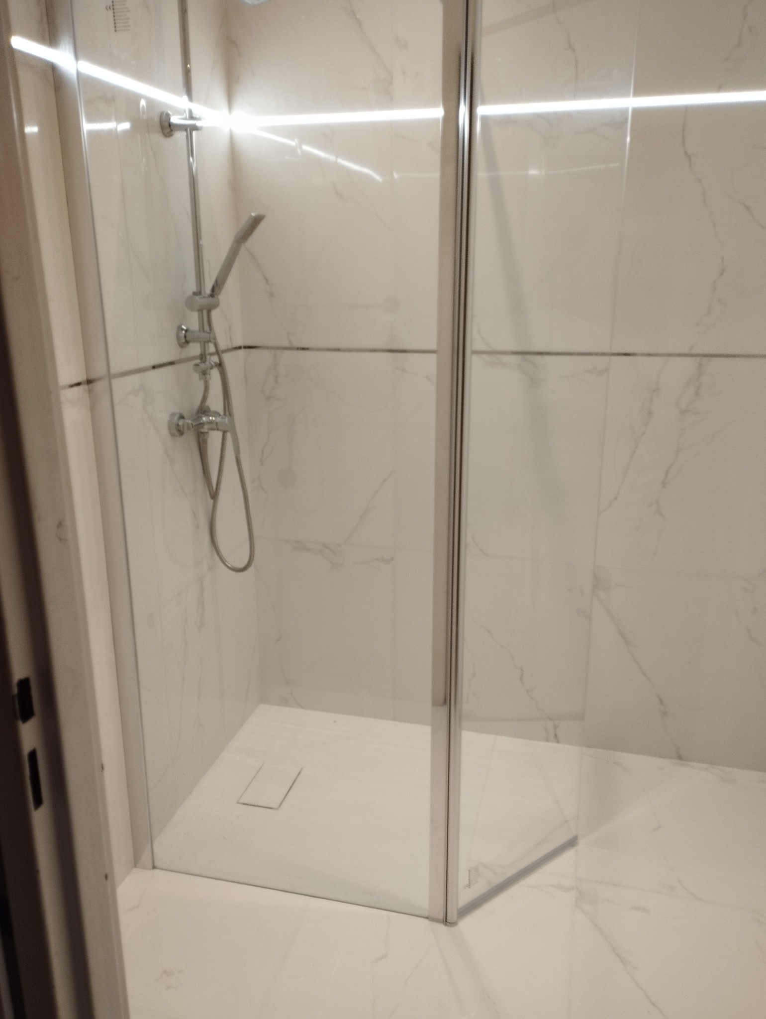 Nowoczesna kabina prysznicowa z chromowaną armaturą na tle białych marmurowych płytek, wykończona ledowym oświetleniem.