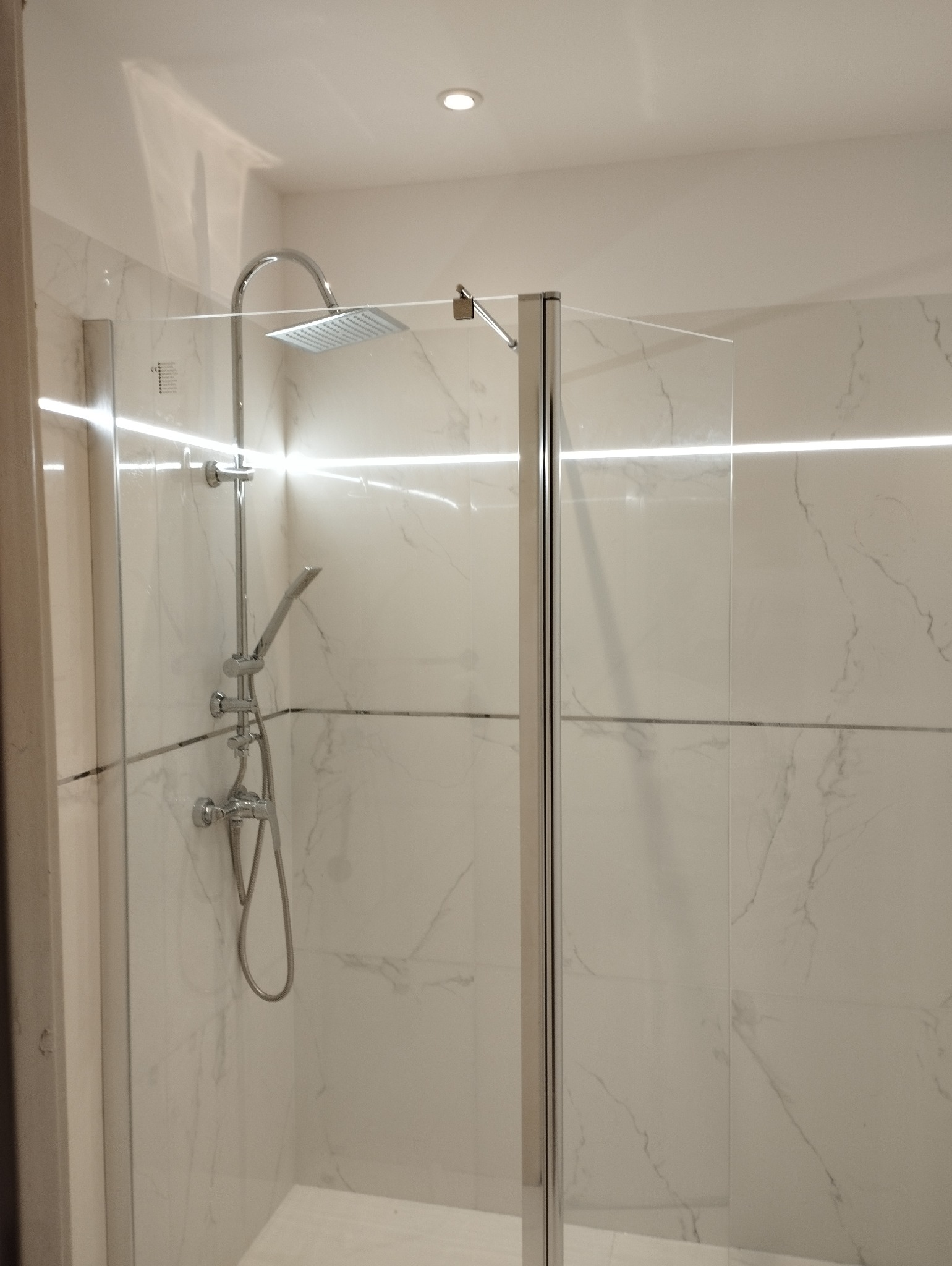 Nowoczesna kabina prysznicowa z chromowaną armaturą i marmurowymi płytkami, akcentowana subtelnym oświetleniem LED. Minimalistyczny design, czyste linie.