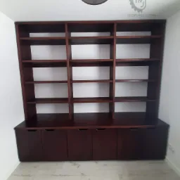 Ciemnobrązowy regał z drewna z szafkami na dole i otwartymi półkami u góry, widok od dołu, na białym tle ściany i jasnej podłodze.